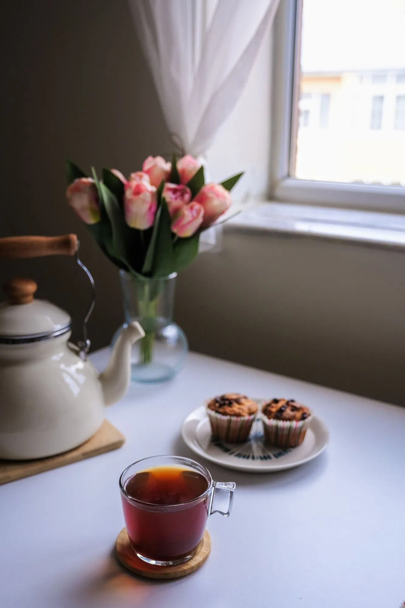 Tea in a glass cup and two muffins on a white table by the window