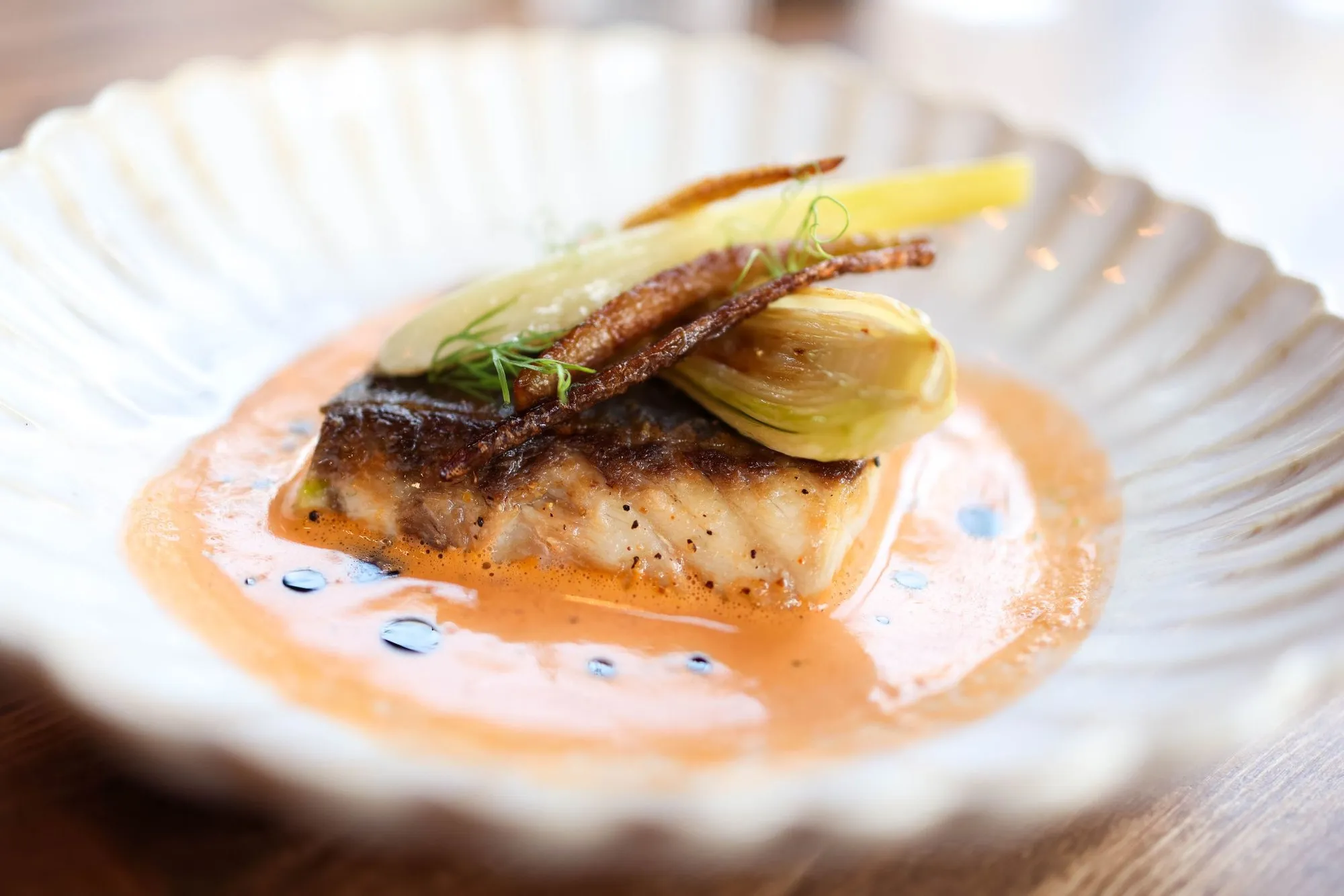 Seared fish on a pale sauce with fennel, on a fluted plate