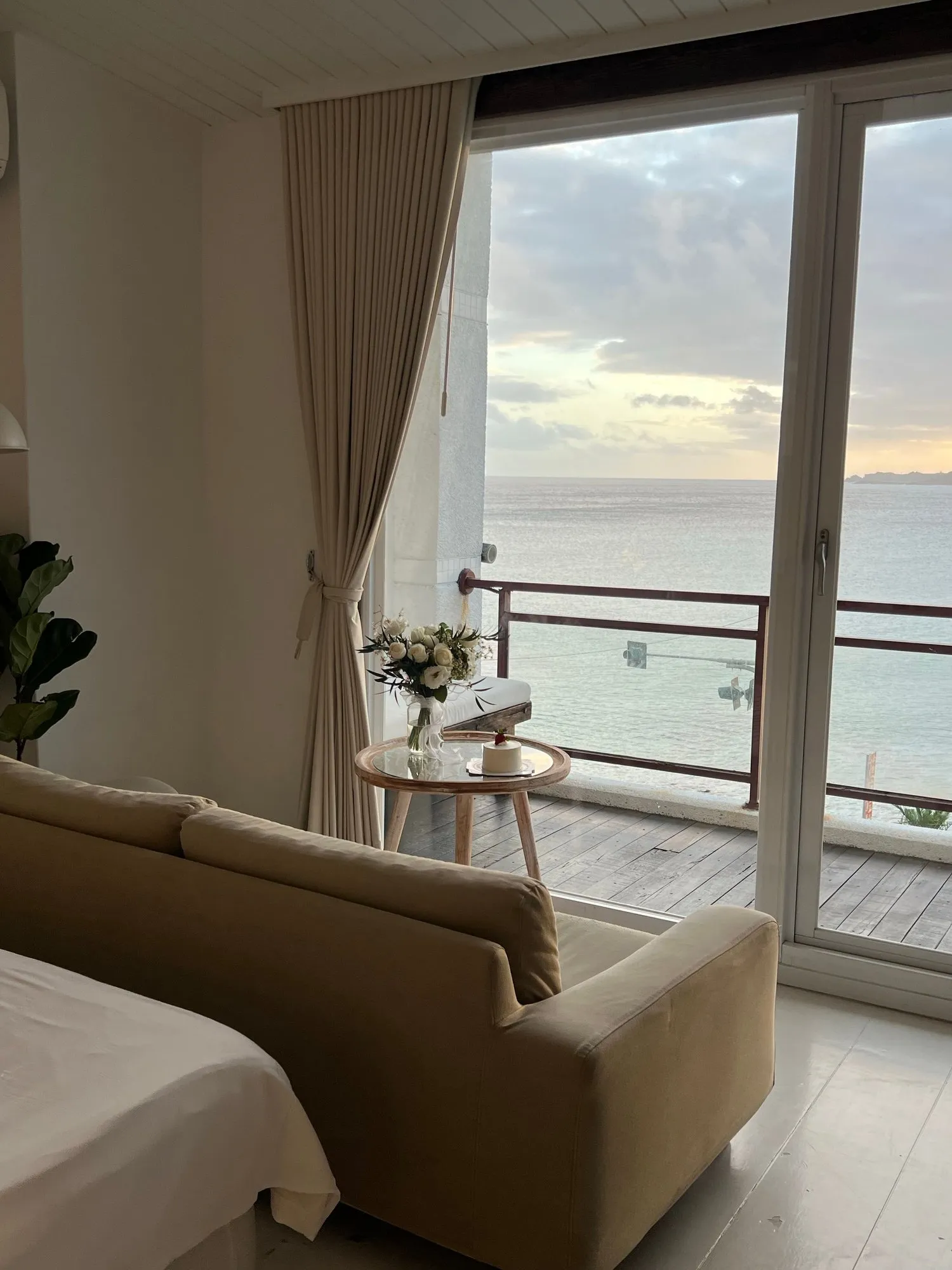 A sofa facing balcony doors onto the sea at sunset